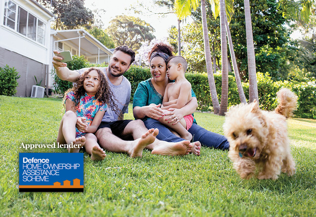 Family sitting on lawn of a suburban front yard.