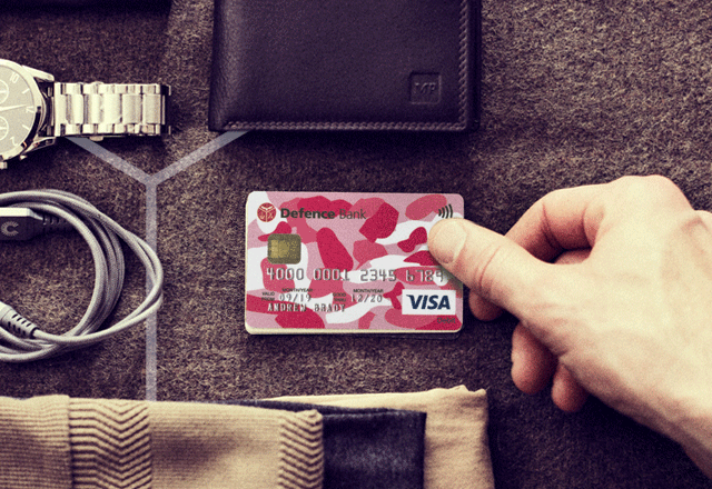 Hand holding pink Defence Bank debit card.