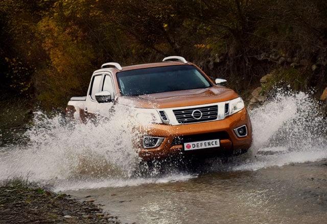 An orange four-door ute parked in a forested setting