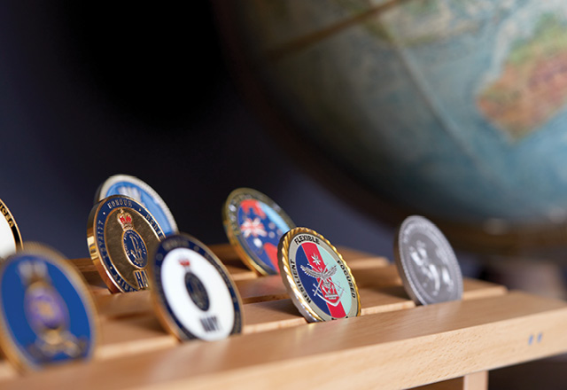 Defence Force challenge coins presented on a timber board in front of a world globe.