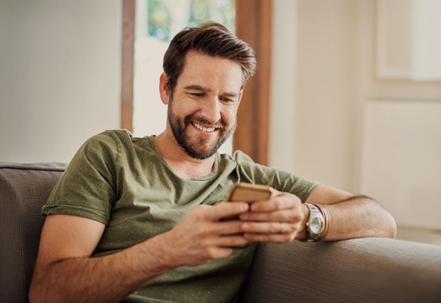 Shot of a happy young man using a mobile phone on the sofa at home